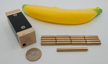 Load image into Gallery viewer, One Peckish Primate, One rubber banana, Sixteen small brass bananas, One large brass banana, and a UK Two Pound Coin.